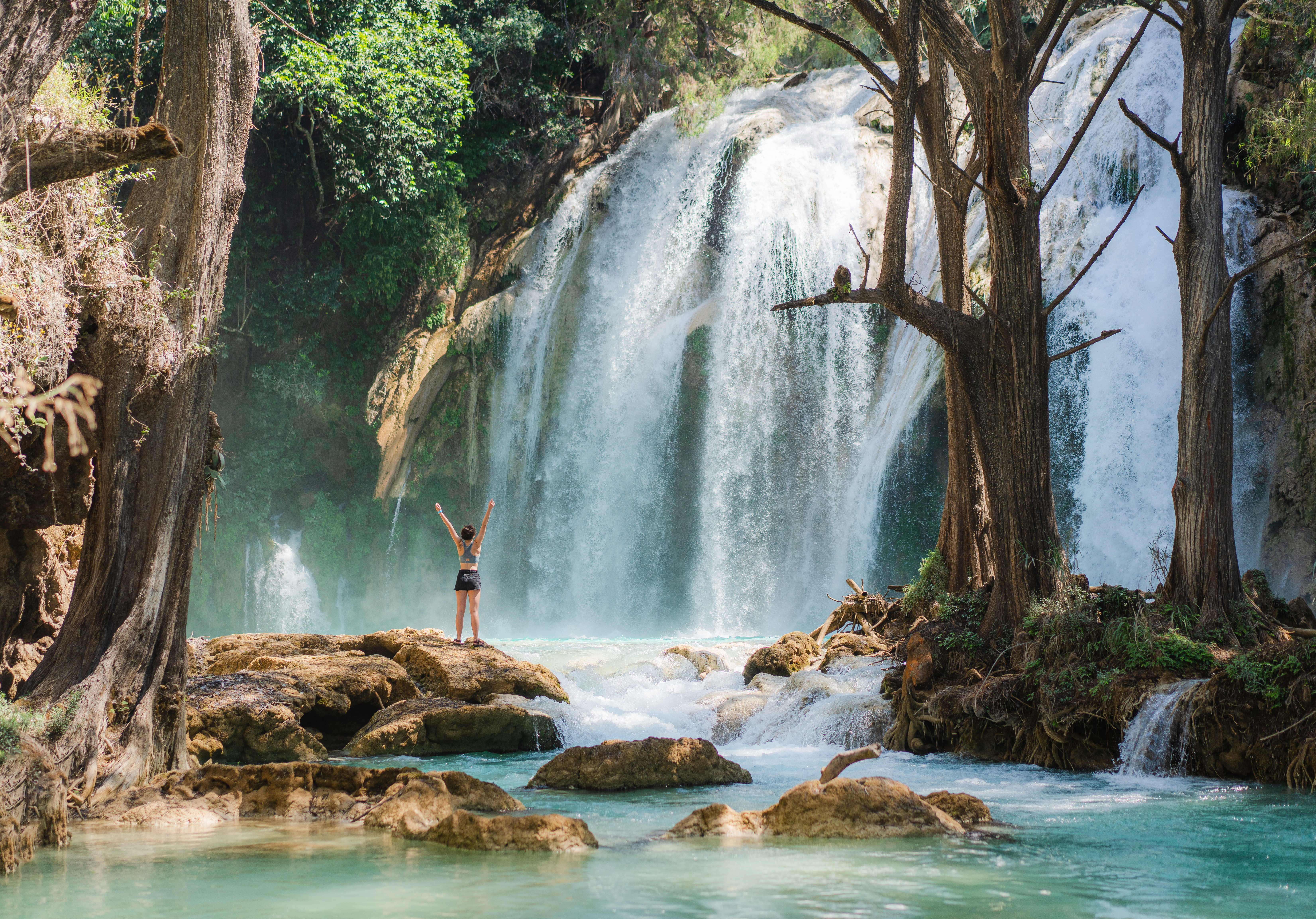 Young Caucasian woman standing near El Chiflon waterfall in Chiapas with her arms raised to the sky