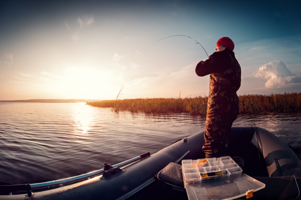 Man fishing from the boat on the lake at sunset