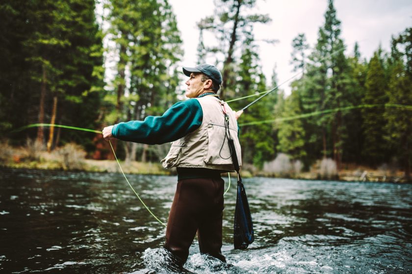 A fly fisherman concentrates as he casts his line in a beautiful stretch of the Metolius River, a tributary of the Deschutes River in Oregon state. Horizontal image with the fly line curling perfectly within the frame.