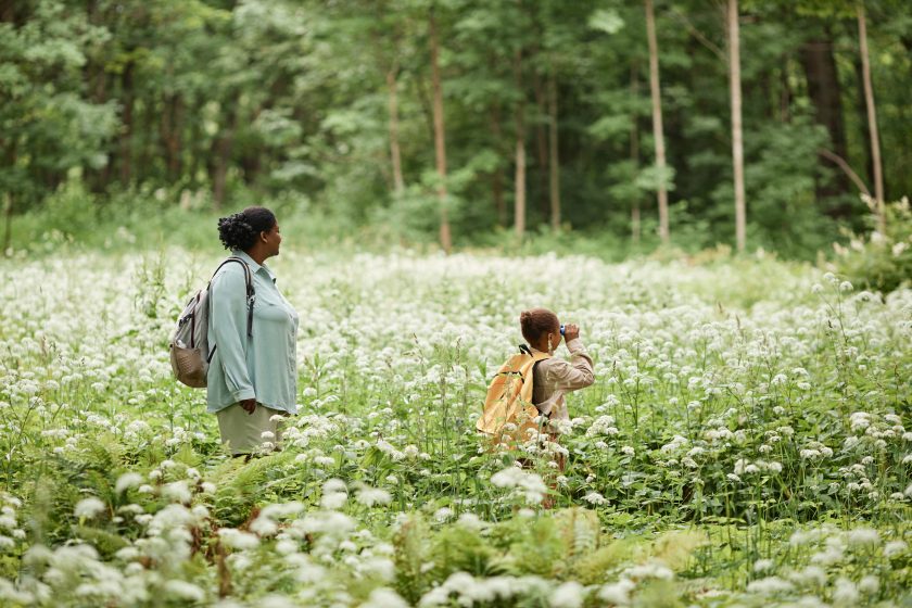 Side view portrait of mother and daughter walking across field of forest flowers while hiking together