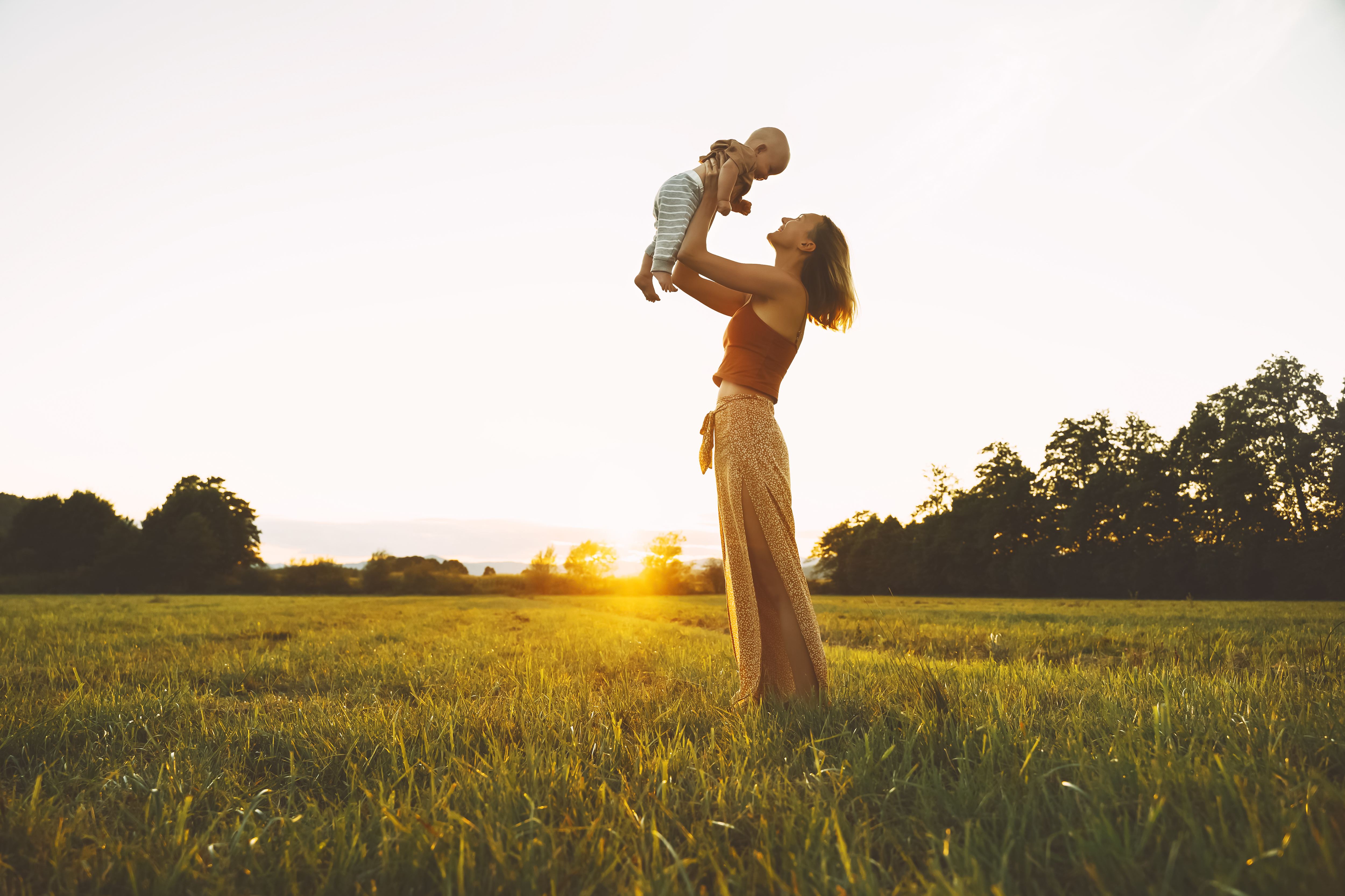 Loving mother and baby at sunset. Beautiful woman and small child in nature background. Concept of natural motherhood. Happy healthy family at summer outdoors. Positive human emotions and feelings.