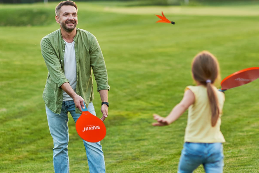 Father and daughter play badminton on the grass.
