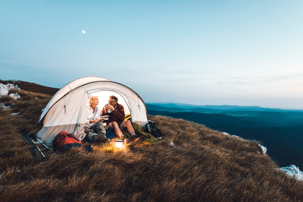 Senior couple camping in the mountains and eating a snack
