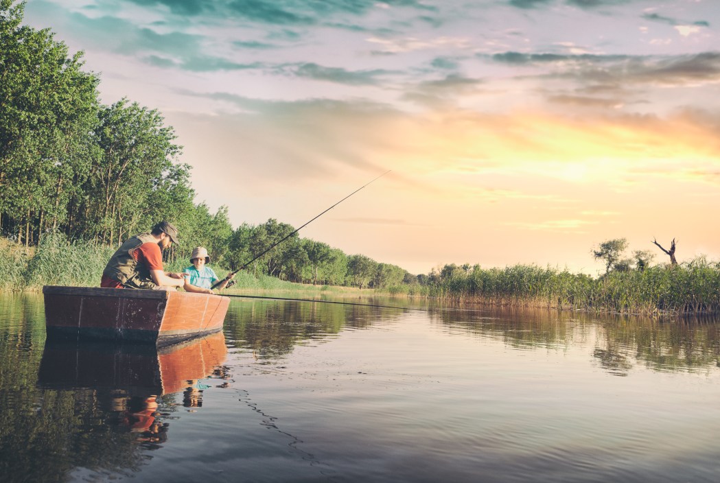 Dad and son sitting in boat and fishing on lake, the boy showing his dad how he caught a fish