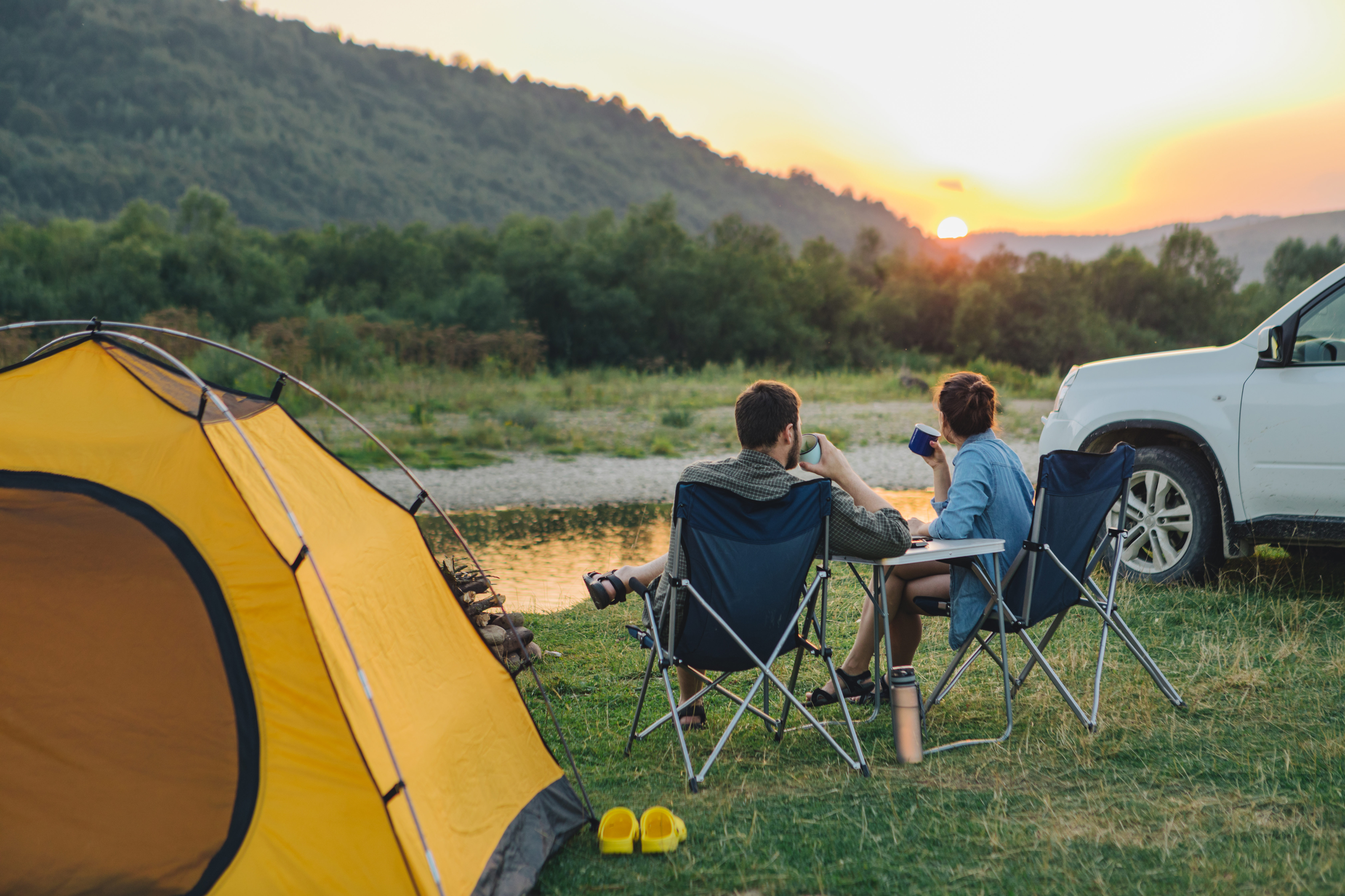 couple sitting in camp chairs looking at sunset above river in mountains. hiking concept.