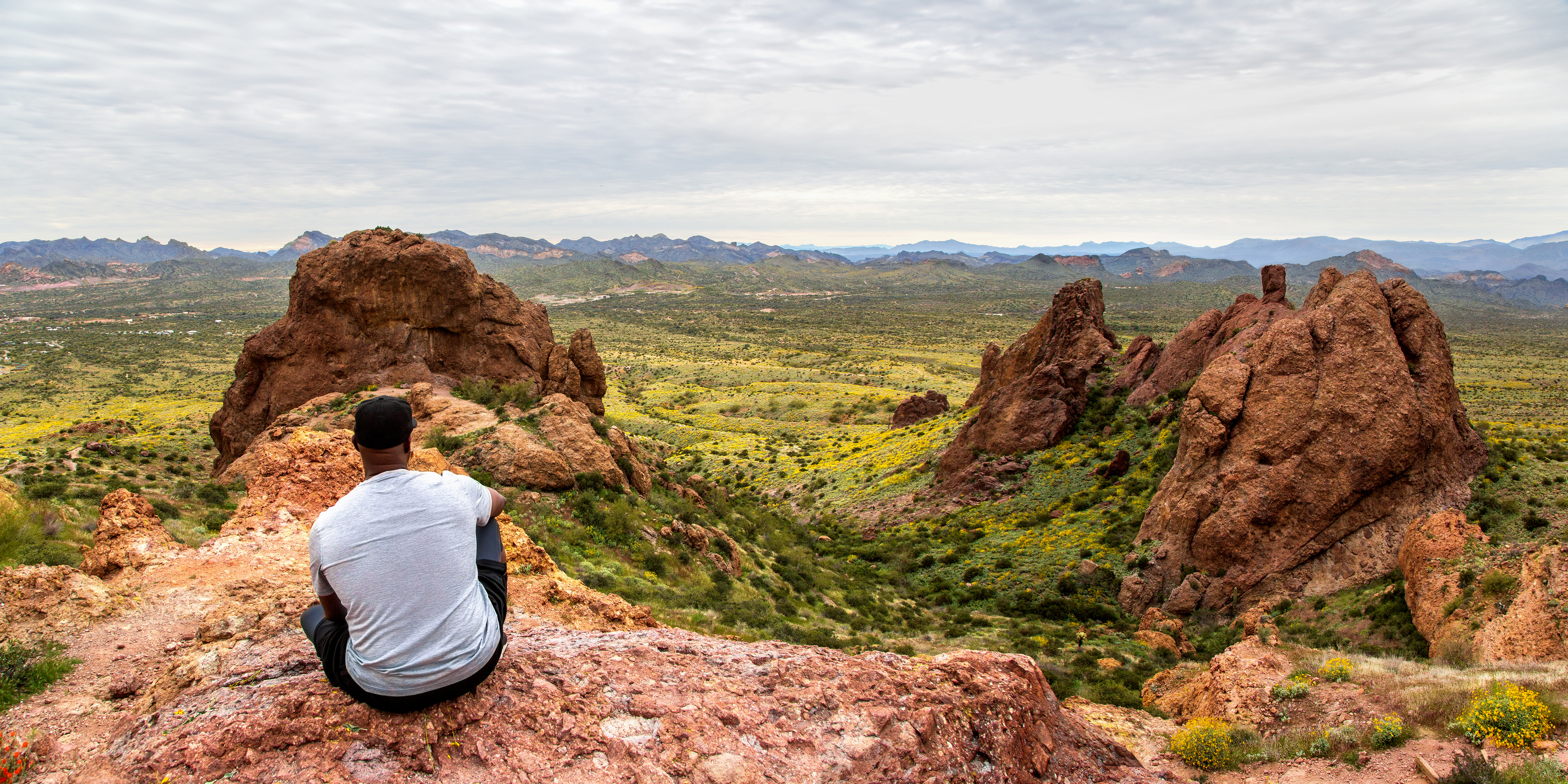 Black man contemplating the view from The Flatiron in the Superstition Mountains from the basin at the top of Treasure Loop Trail. Hiking in the Arizona desert panoramic. Moutain peak hike banner.