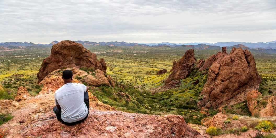 Black man contemplating the view from The Flatiron in the Superstition Mountains from the basin at the top of Treasure Loop Trail. Hiking in the Arizona desert panoramic. Moutain peak hike banner.