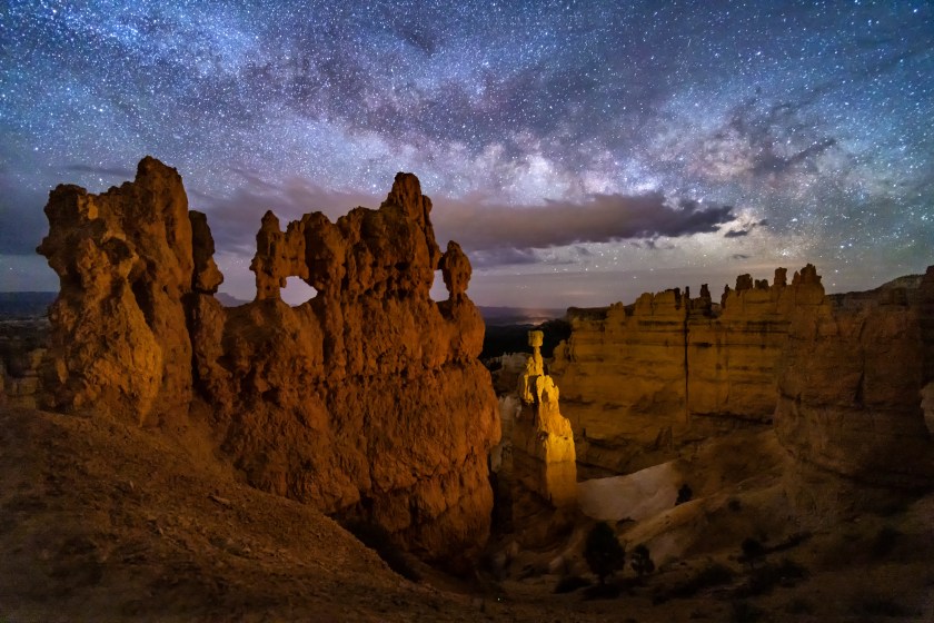 A hoodoo with small windows and Thor's Hammer against a night sky with clouds and the Milky Way below Sunset Point in bryce Canyon National Park, Utah.