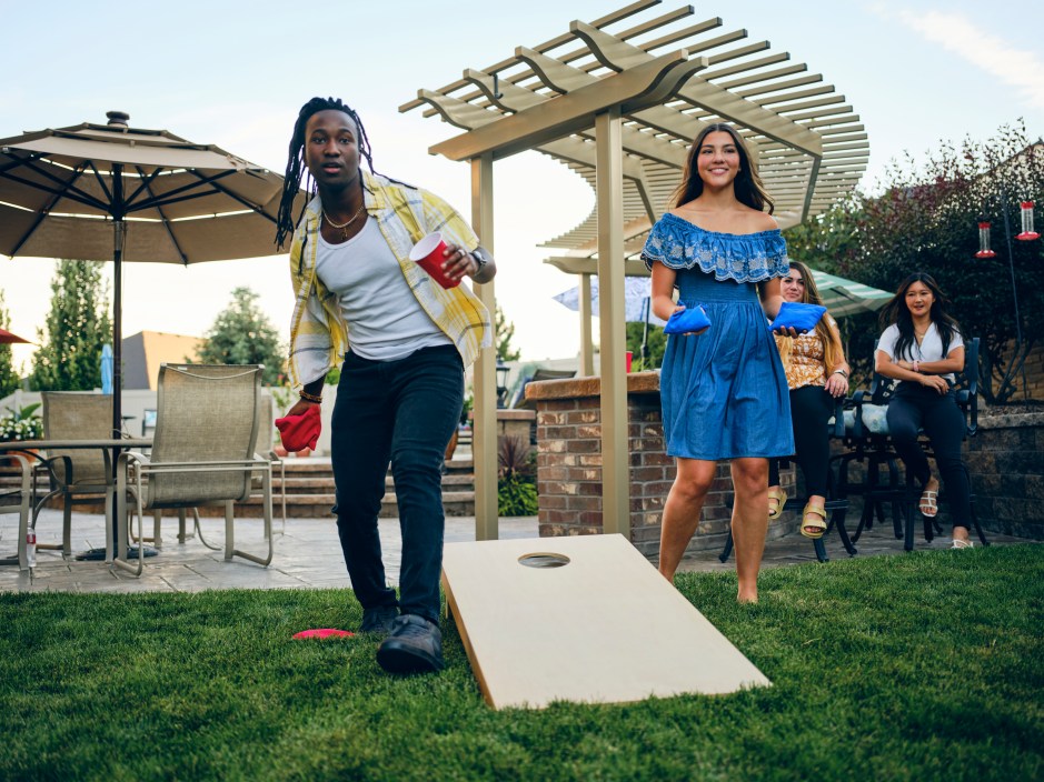 A group of friends playing a Cornhole bean bag toss game in a backyard of a home.