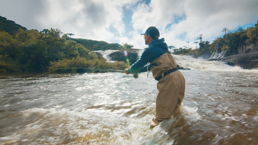 Fisherman fly fishing in rapid river for high water flow