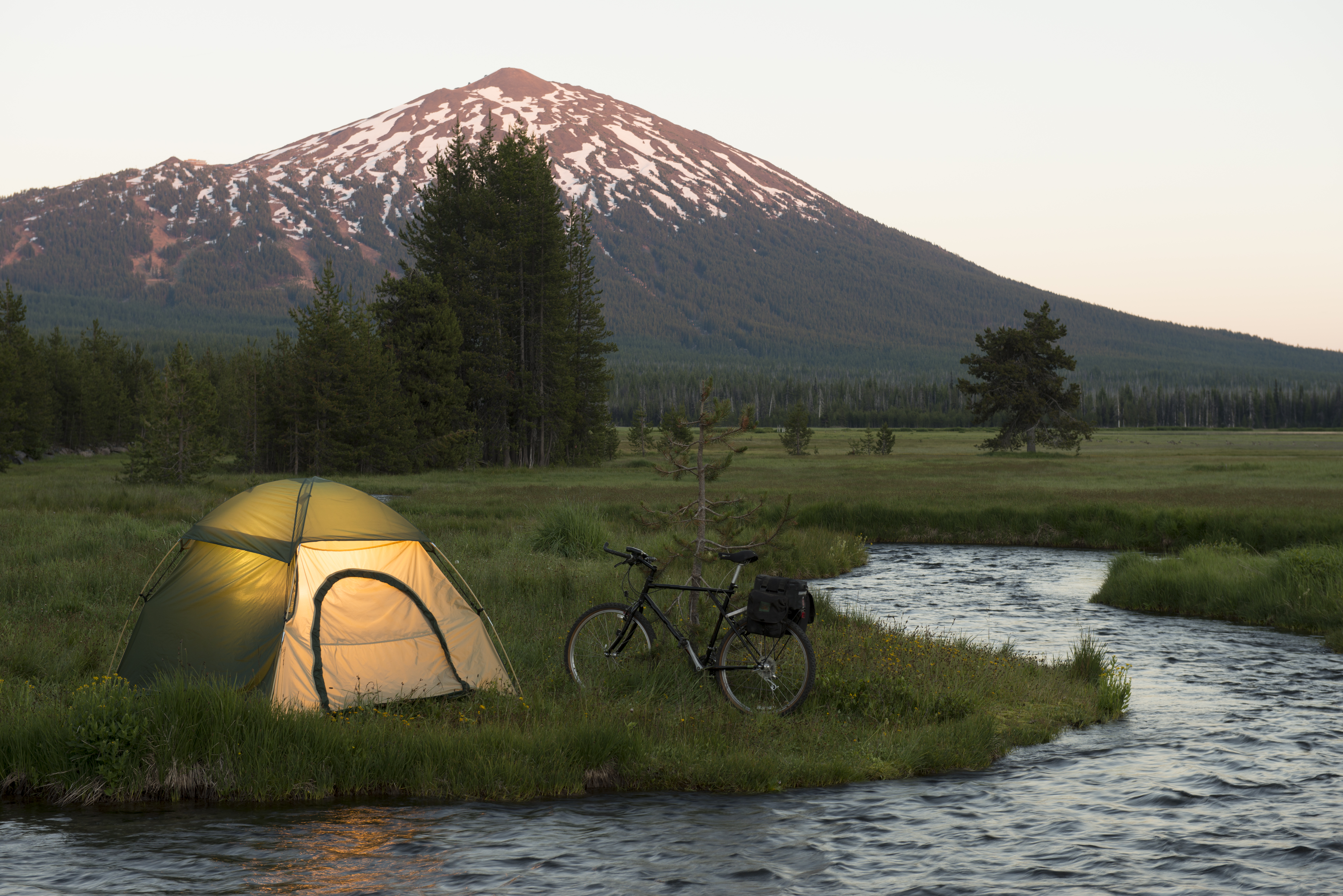 This image shows an alpine meadow w/illuminated tent after a day of road biking. Mt Bachelor in background. Pacific northwest cascades.