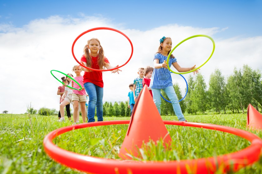 Two group of kids playing with colorful hoops and throw them on cones while competing with each other during summer sunny day
