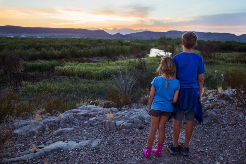 A caucasian brother and sister enjoying a sunset overlooking the Rio Grande in a valley in Big Bend National Park. 