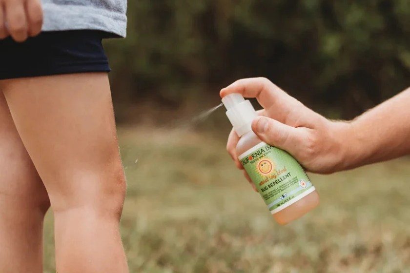 Adult spraying California Baby Natural Bug Blend Repellent onto child's leg