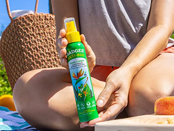 Person sitting down in the grass, holding a bottle of Badger Anti-Bug Shake & Spray Mosquito Repellent