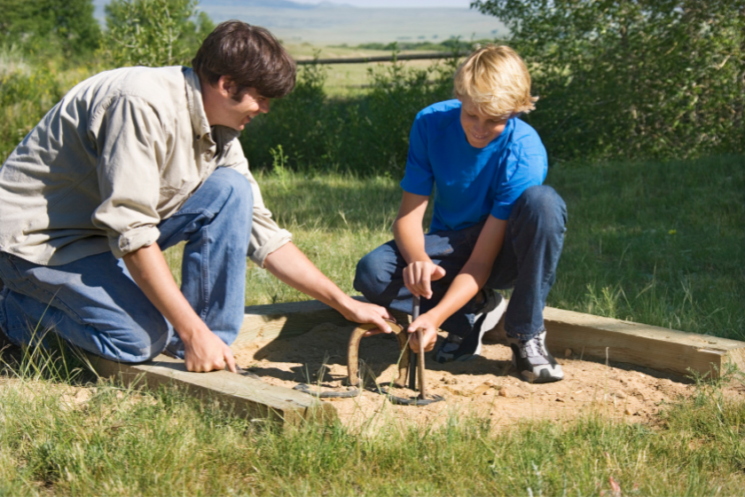 Two boys hammering in a horseshoe stake. 