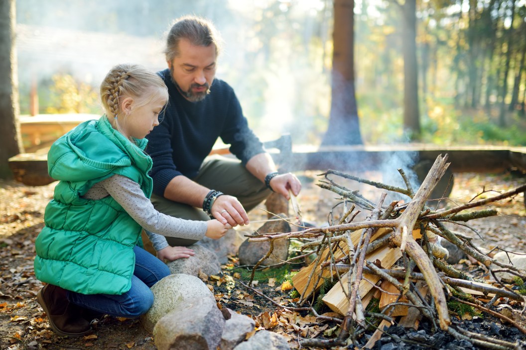Young girl learning to start a bonfire from her father.