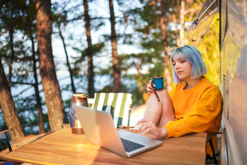 Young Woman using laptop while drinking coffee at camping