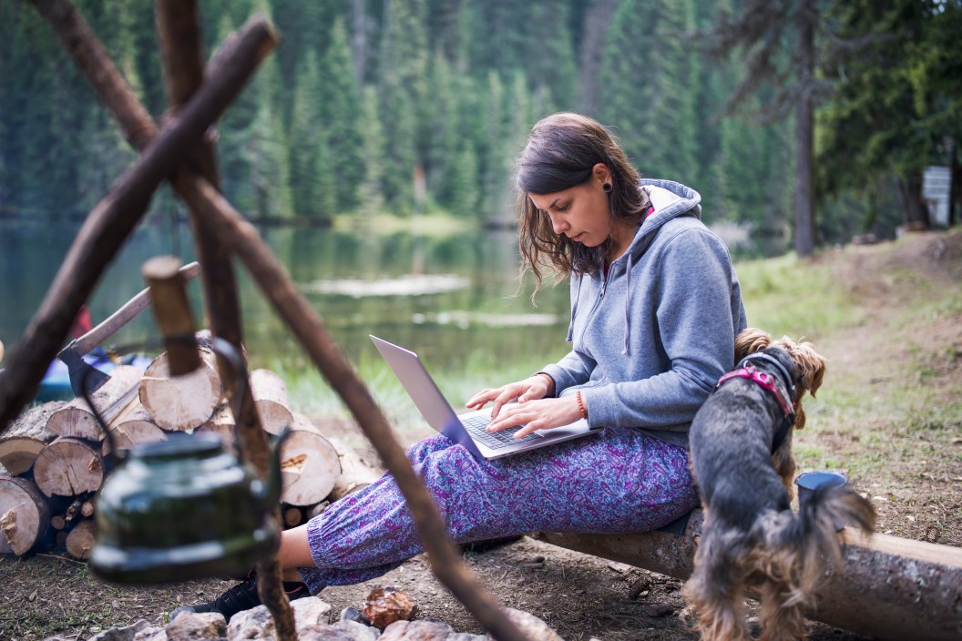 A shot of a young woman working on her laptop while camping in the nature.