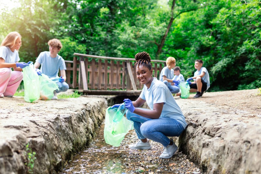 Nature cleaning, volunteer ecology green concept. Young woman pick up river at sunset . Environment plastic pollution. Side view of a woman in protective gloves putting household waste into bag.