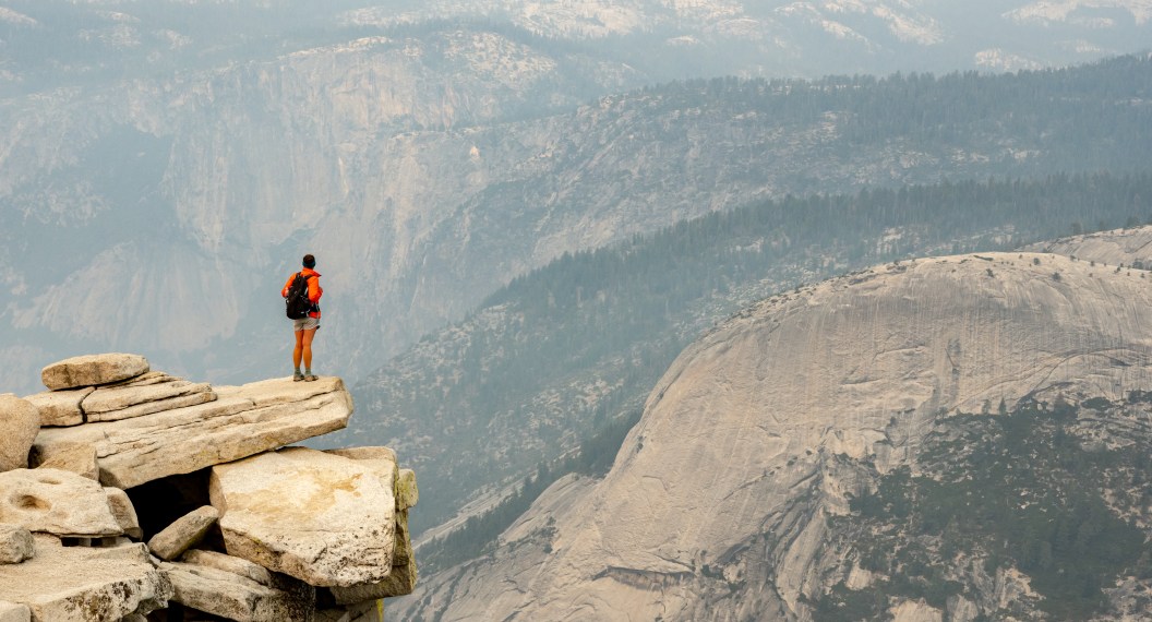 Woman Looks Out Over Smoky Yosemite Valley Below from the summit of Half Dome