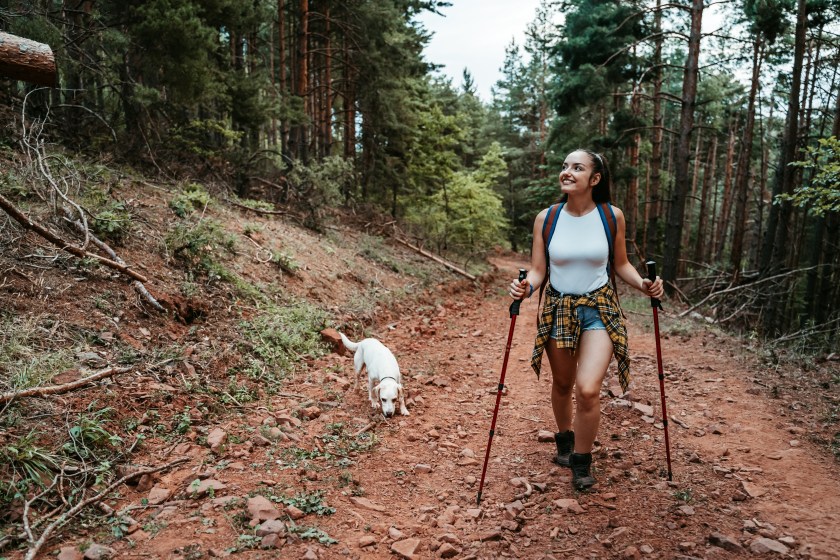 Beautiful young woman hiking on the trail in the forest with her dog.