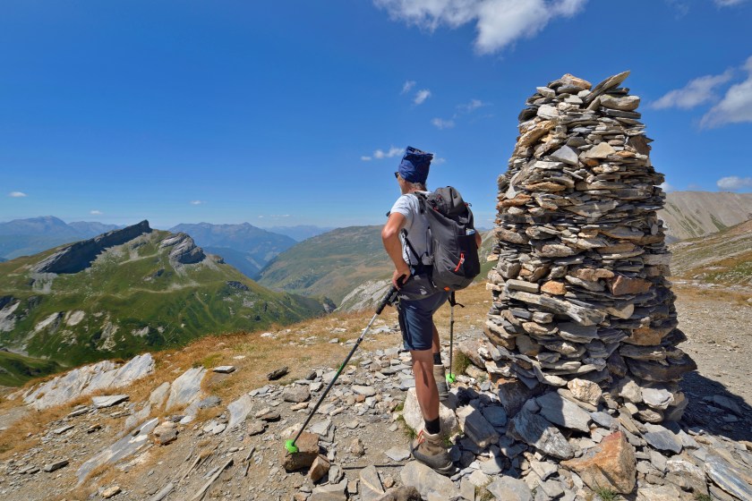 hiker standing and overlooking the mountains a hiking trail next to a big cairn the tour of Mont Blanc in summer