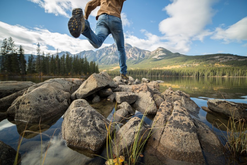 Hiker jumps rock to rock in mountain lake. Low angle view.