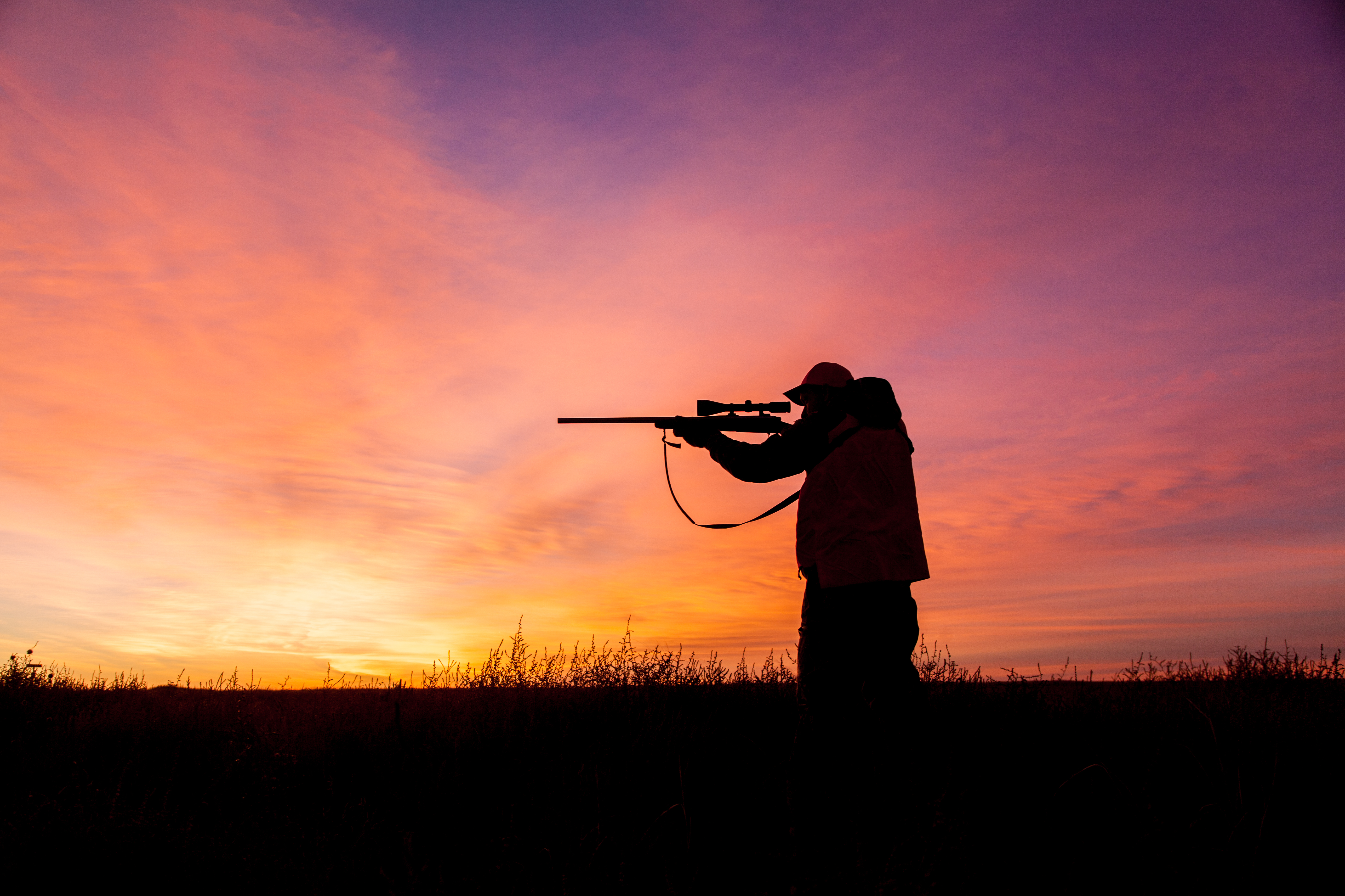 a hunter with rifle shouldered silhouetted in the sunrise