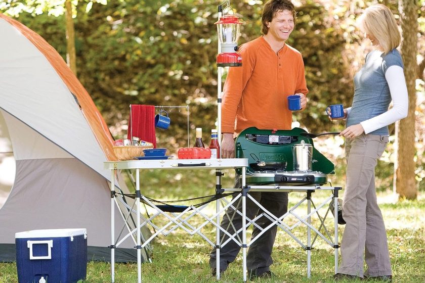 Coleman Pack-Away camp kitchen at a campsite with two people.
