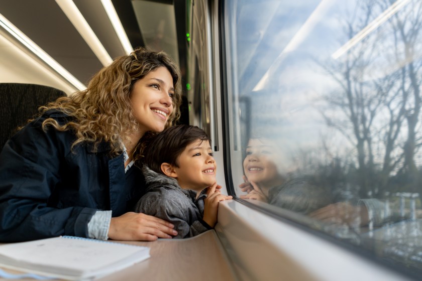 Happy single mother and son looking at the window view both smiling while traveling by train