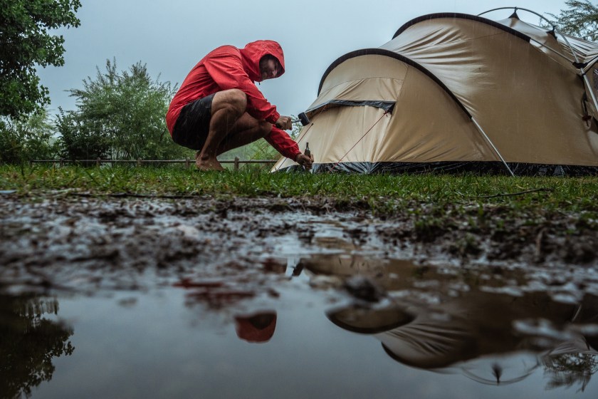 Man camping fixing tent on rainy day