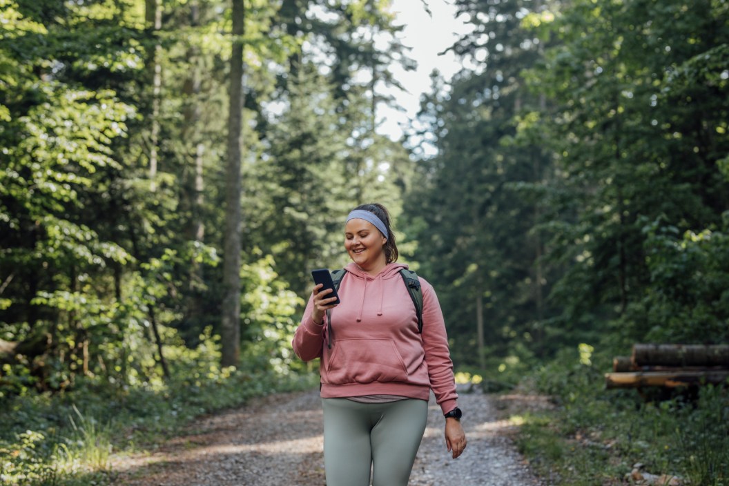 Back to nature: a happy young Plus Size woman spending the day outdoors and taking photos with her smart phone.