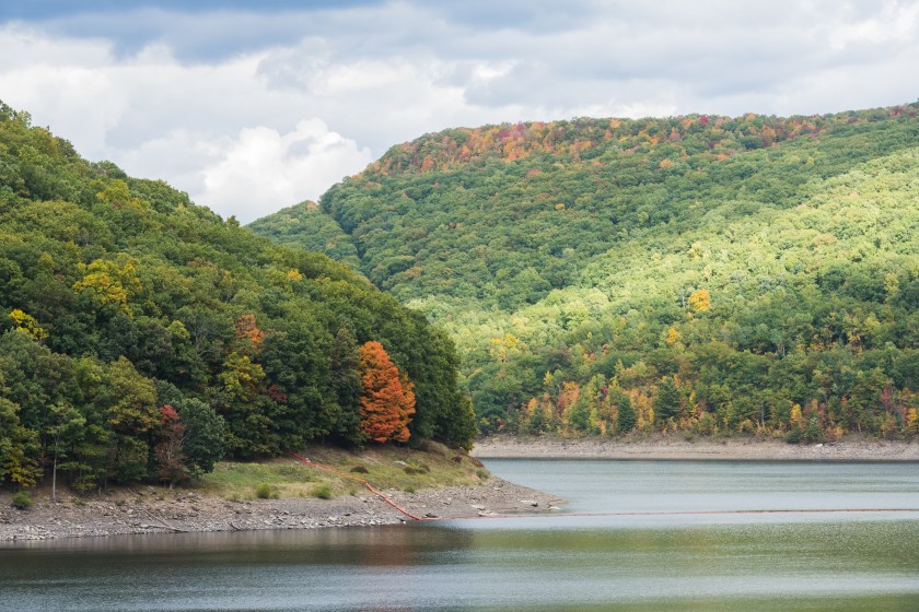 A landscape of a curve in the river water flowing around a bend of mountains covered with trees at the Allegheny Reservoir on a cloudy, autumn day in Pennsylvania, USA.