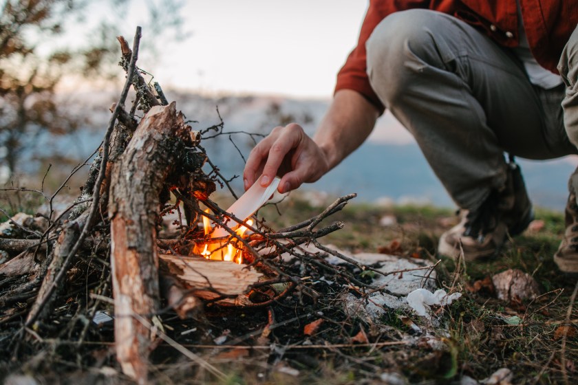 Medium shot of a hiker setting a fire with paper and firewood