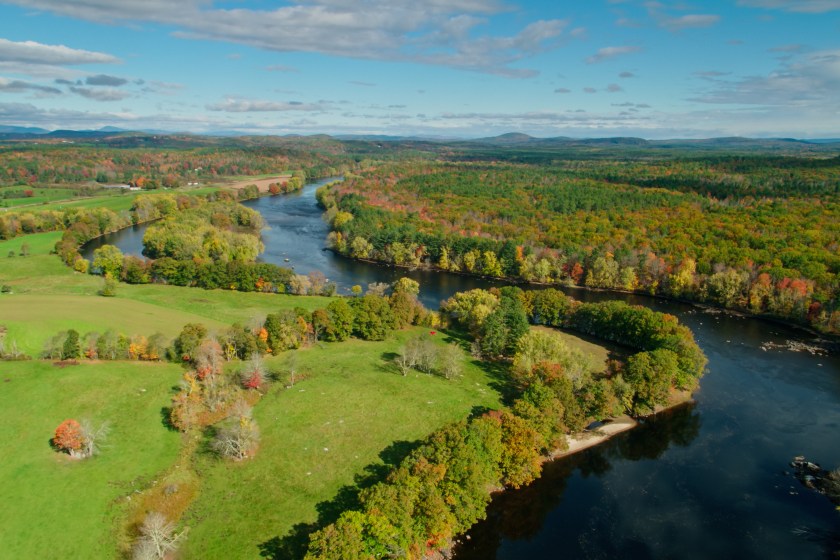 Aerial shot of Androscoggin River flowing past forest and farmland near Turner, Maine on a clear sunny day in autumn.