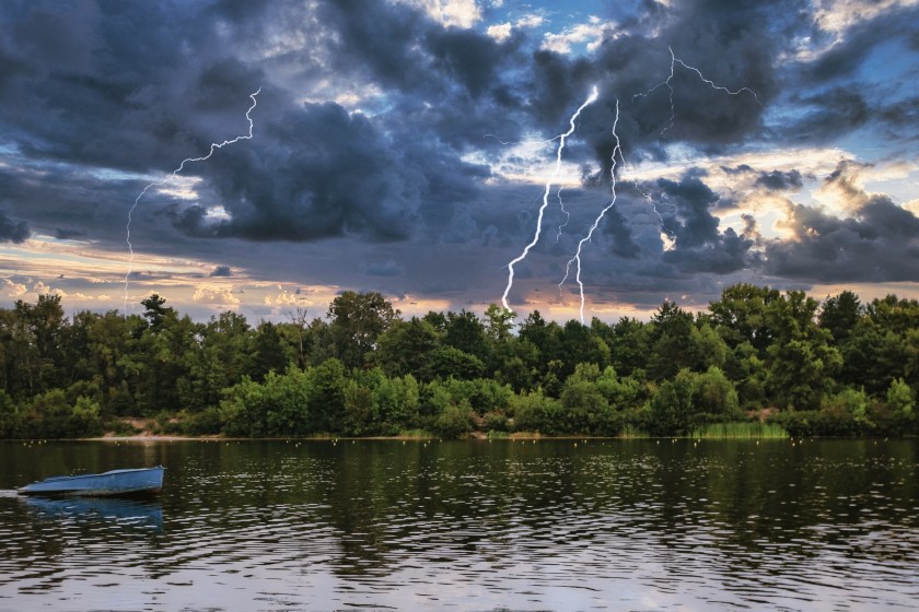 A forest lake under thunderclouds with lightning.