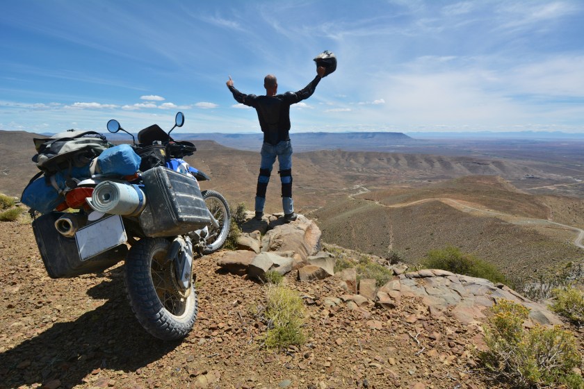 motorcyclist stands next to his motorcycle and appreciates the view over the karoo, south africa.