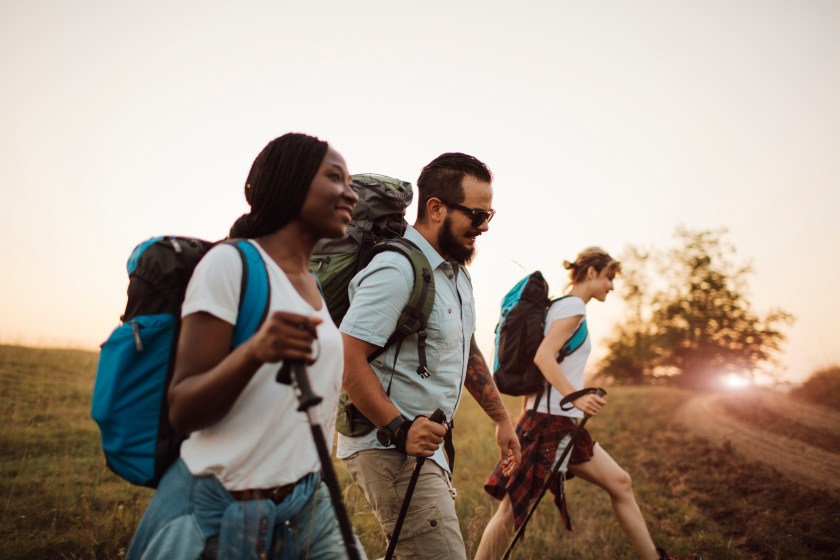 Group of young hikers, walking together. They are carrying backpacks and hiking poles. Enjoying in the nature and healthy lifestyle. Side view.
