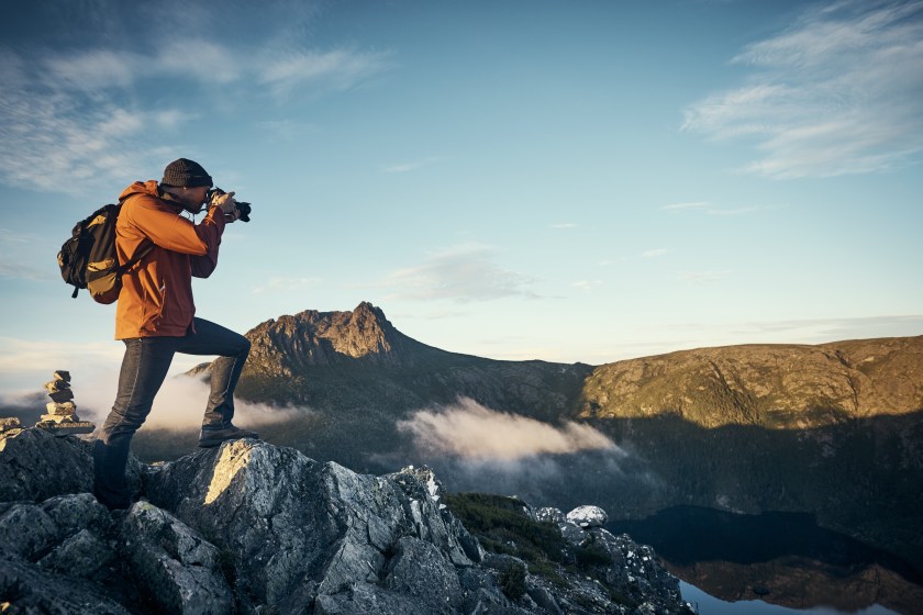 A young man taking photographs while hiking in the mountains.