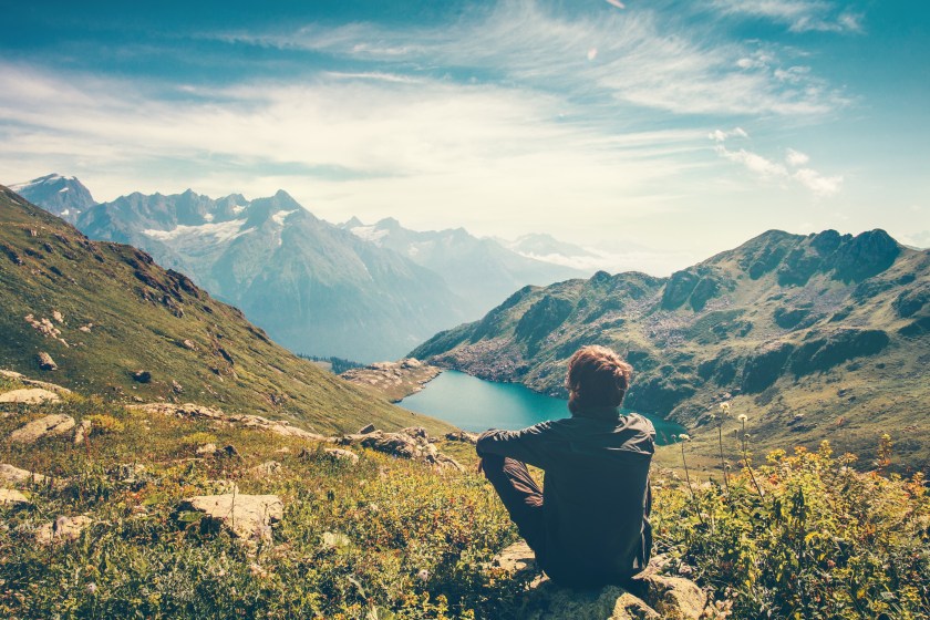 A man meditating in the mountains with a serene view of a lake.