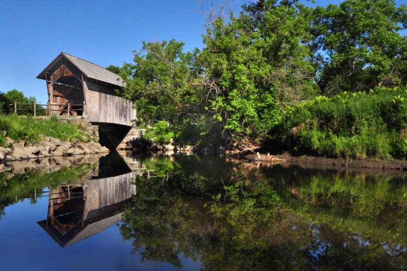 A covered bridge crosses the Winooski River in a pasture.