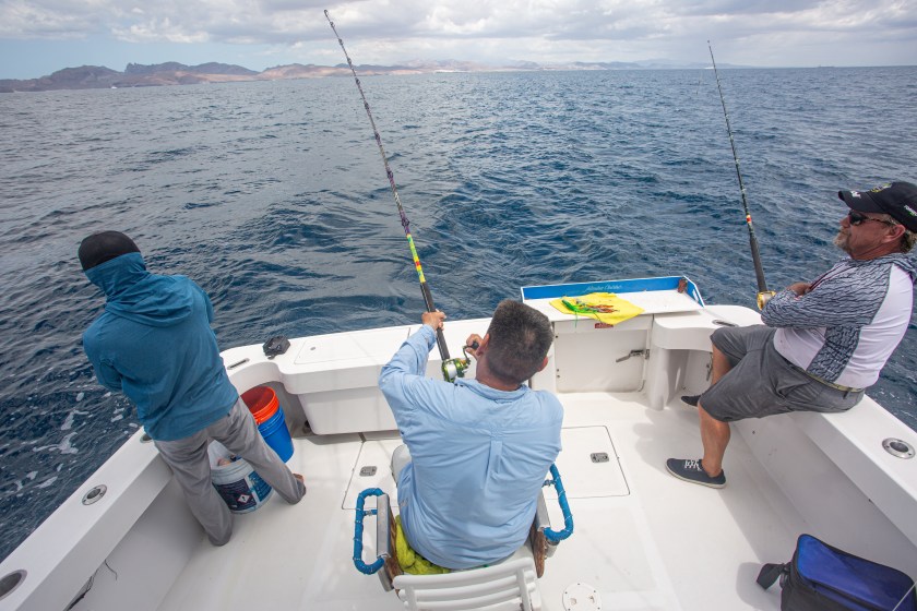 3 people fishing on a small white boat in the water