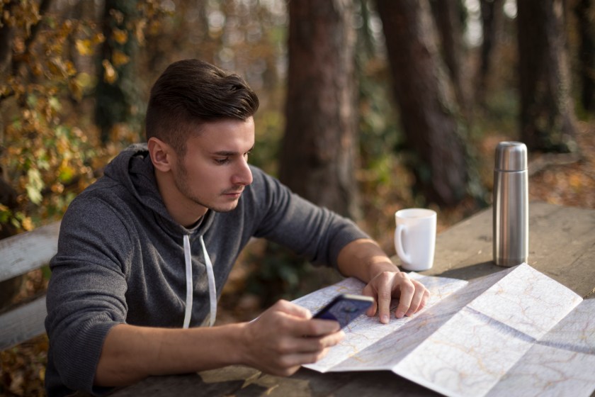 man outdoors references a map on a table
