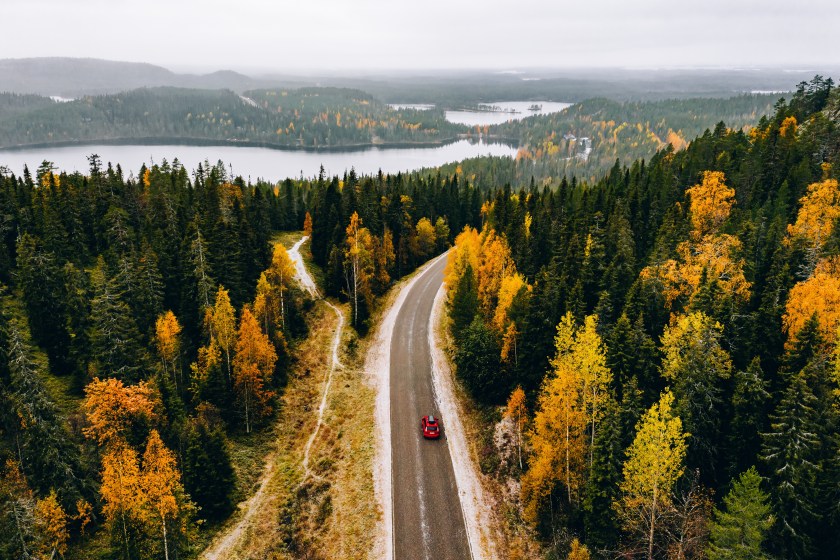 Aerial view of first snowy autumn color forest in the mountains and a road with red car in Finland Lapland.