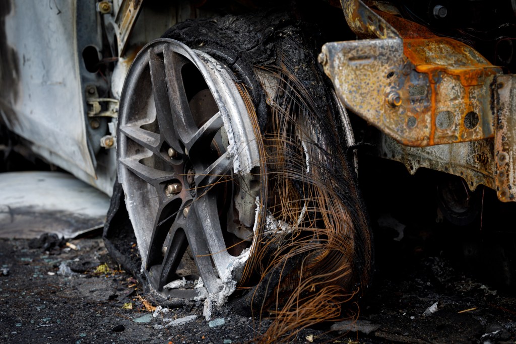 Wheel of burned car.Burnt flat tire on the car is on the gray asphalt road. Close up