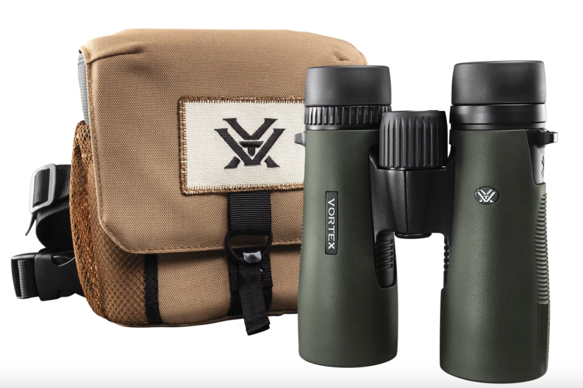 A product photo of dark green binoculars in front of a canvas bag 