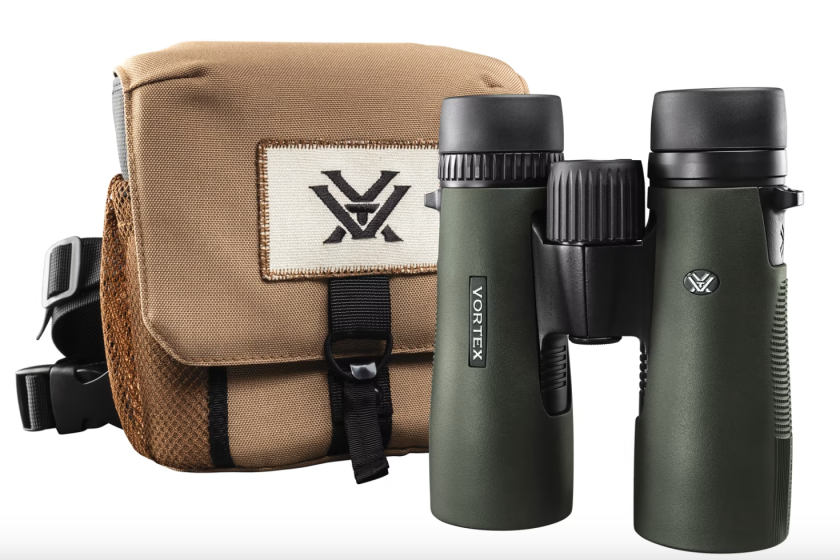 A product photo of dark green binoculars in front of a canvas bag