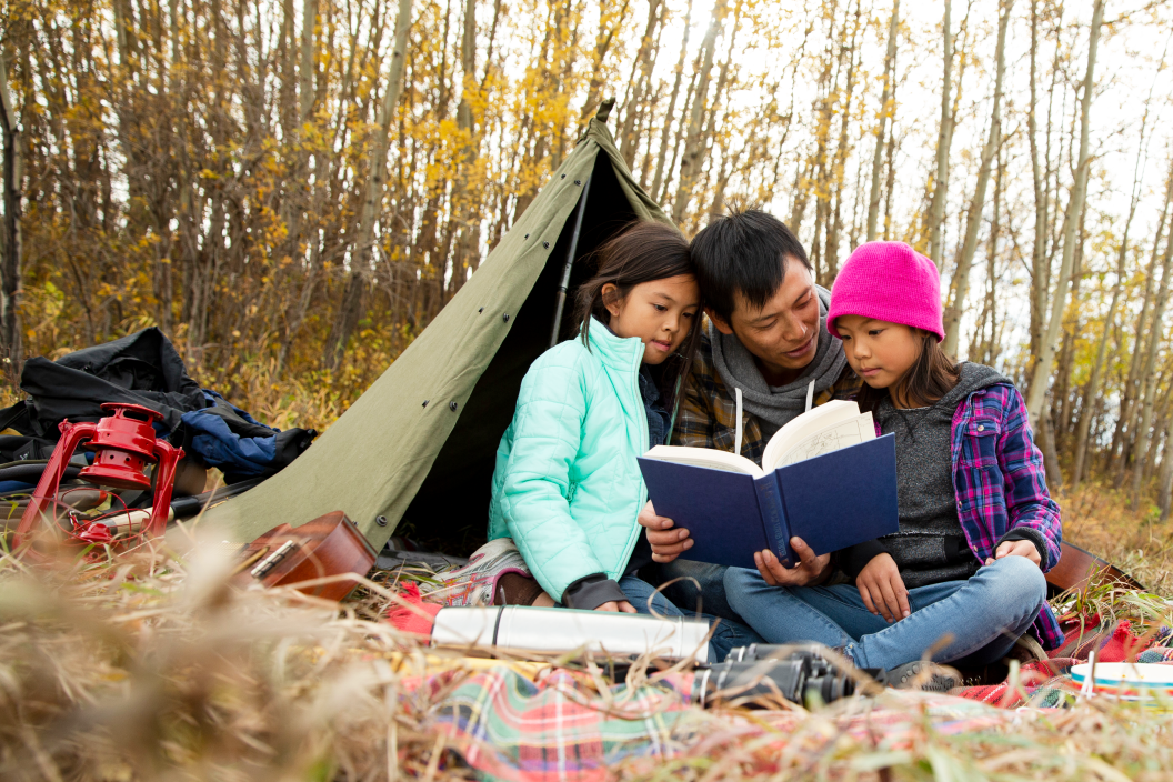 family with father and kids reading outside while camping