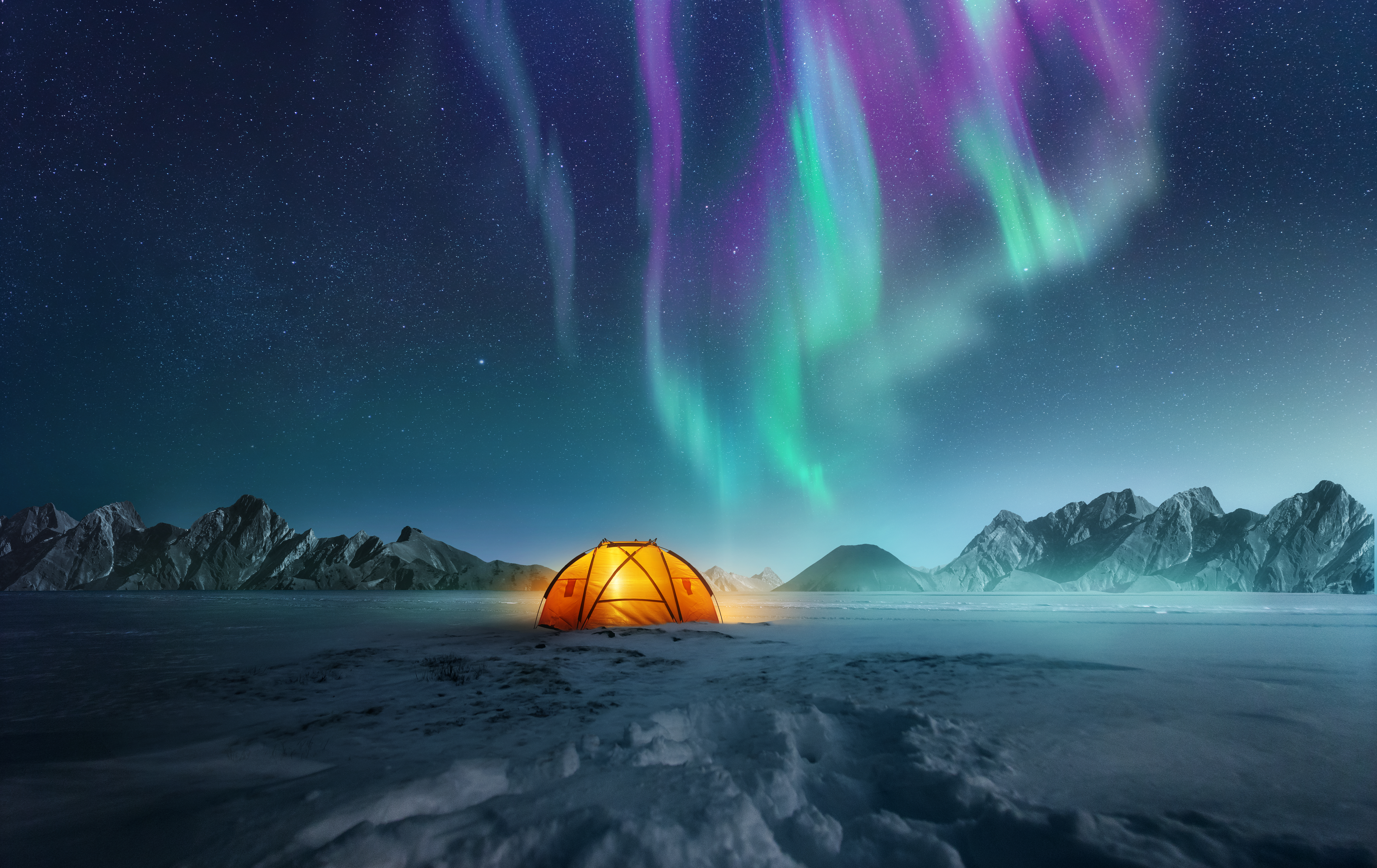 A tent pitched up in snow at night with the northern lights flickering in the sky above. Aurora Borealis and travelling. Photo composite.